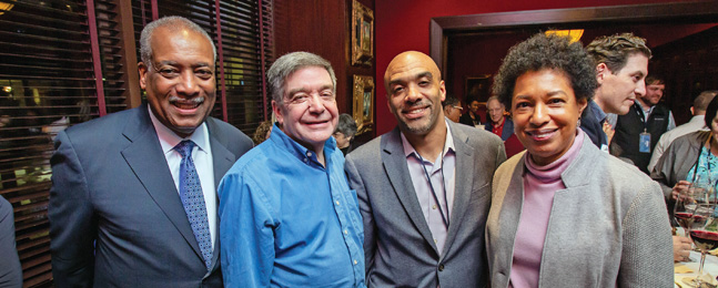 Four smiling people stand shoulder to shoulder